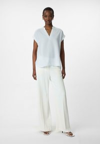 Witte gestreepte blouse met kraag en korte mouwen, gecombineerd met witte wijde broek en gestructureerde hoge hakken, tegen een neutrale achtergrond.