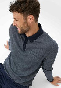 Marineblauwe en grijze, gestreepte poloshirt met lange mouwen, een effen kraag, drie knopen en een borstzak. Zacht, gekreukt materiaal.