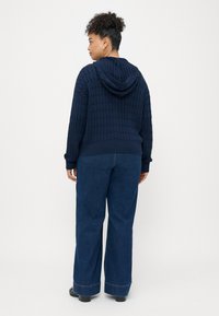 Ναυτικό πλεκτό hoodie με υφή, χαλαρή εφαρμογή, ριμπ μανσέτες και στρίφωμα. Συνδυάζεται με φαρδιά τζιν παντελόνια σε σκούρο χρώμα και μαύρα παπούτσια.