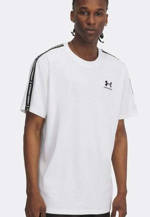 Uomo che indossa una maglietta bianca Under Armour con il logo nero sul petto e strisce nere con il marchio sulle spalle e sulle maniche.