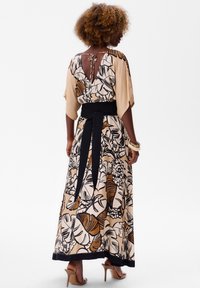 Maxi-jurk met een bloemenprint in beige, bruin en zwart. Heeft een V-rug, brede mouwen en een zwarte tailleband. Soepele stofstructuur.