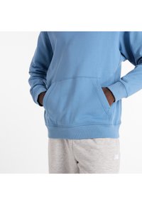 Sudadera azul claro con un bolsillo canguro, puños y dobladillo acanalados, combinada con pantalones deportivos grises que tienen un logotipo blanco. Textura suave.
