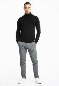 Črna turtleneck pulover, prilegajoča zasnova, v kombinaciji z sivimi slim-fit hlačami in belimi supergami. Preproste, čiste linije in nevtralne barve.