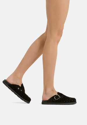 Legs wearing black slip-on shoes with small studs and a buckle, shown walking against a plain white background.