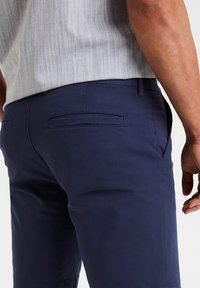 Pantaloni corti in cotone blu navy con una texture liscia, dotati di tasche laterali e posteriori. La vita presenta un passante per la cintura e una leggera lucentezza.