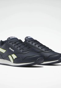 Mörkblå sneakers i syntetmaterial med vit sula, kontrasterande gula ränder, rund tå och snörning med Reebok-logotyp.