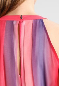 Top sans manches en tissu transparent présentant un dégradé de teintes roses à violettes, avec une fermeture par bouton à l'arrière et un détail de trou de serrure.