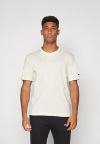 Cremfarbendes T-Shirt mit kurzen Ärmeln, das ein gesticktes "Champion"-Logo auf der Brust trägt, aus weichem Material mit Rundhalsausschnitt.
