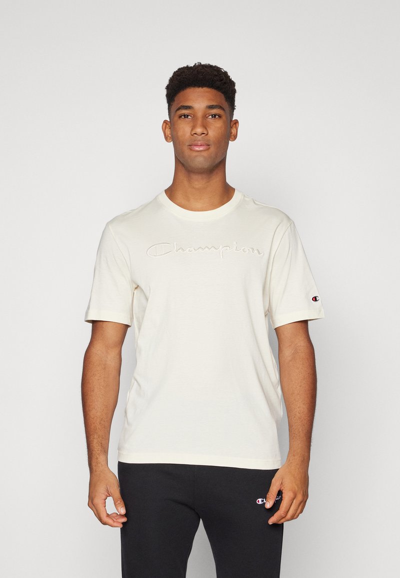 Cremfarbendes T-Shirt mit kurzen Ärmeln, das ein gesticktes "Champion"-Logo auf der Brust trägt, aus weichem Material mit Rundhalsausschnitt.
