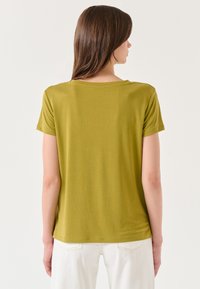 Olijfgroen T-shirt met korte mouwen, in een ruime pasvorm en met een ronde hals, gemaakt van zachte, lichtgewicht stof. Glad textuur, minimale naden.