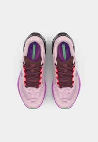 Zapatillas deportivas de color rosa claro con parte superior de malla, detalles morados, suela negra y cordones de colores. Cuentan con un cuello acolchado y un diseño texturizado.