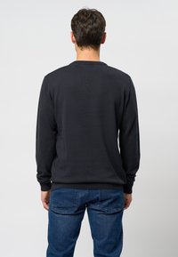 Svart crew-neck sweatshirt med långa ärmar, ribbade muddar och midja. Tillverkad av ett mjukt, texturerat tyg. Bärs med blå jeans.