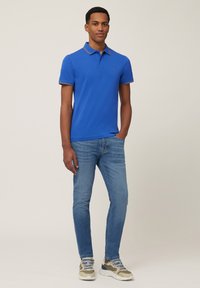 Blue polo shirt with contrasting collar, paired with light blue jeans. The shirt features a subtle logo on the chest and a classic fit.