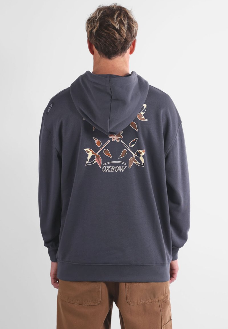 Hoodie gris foncé avec une capuche à cordon, arborant un design floral et le texte "OXBOW" imprimé au dos. Tissu doux et texturé.