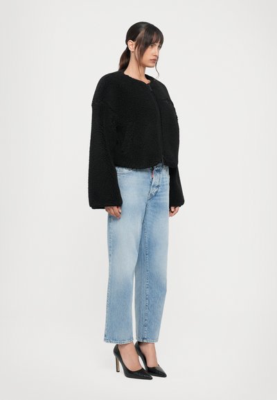Veste noire, fluffy, courte avec un col rond et des manches larges, associée à un jean bleu clair, ample, et des talons hauts noirs.