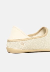 Beige slip-on shoe with a textured fabric upper, soft beige trim, and a flexible light-colored sole; features subtle stitching detail.