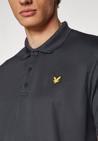 Dark gray polo shirt with a soft texture, featuring a yellow embroidered bird logo on the left chest and three black buttons at the collar.