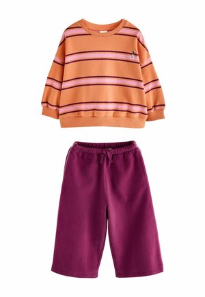 Orange og lyserød langærmet top med små dyredetaljer, parret med mørkelilla shorts med snøre.