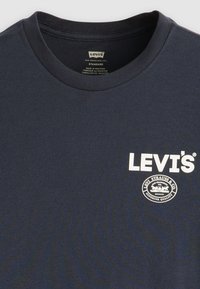 Jūras zila kokvilnas T-kreklu ar apaļu kaklu, kas rotāts ar baltu "Levi's" logo un mazu apļa grafiku uz krūšu daļas. Mīksta tekstūra, standarta izmērs.