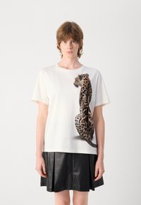 T-shirt en coton blanc avec un grand imprimé léopard sur le côté, à manches courtes et coupe décontractée, associé à une jupe en cuir noir.