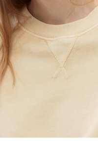 Sudadera beige claro con un cuello redondeado, puños acanalados y un detalle de 'V' cosido en el cuello, fabricada con un tejido suave y texturizado.