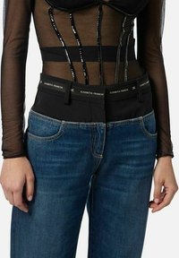 Top nero in rete a maniche lunghe con accenti verticali lucidi, abbinato a jeans di denim azzurro con una fascia in vita nera e tasche frontali.