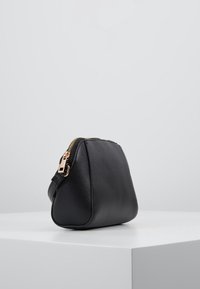 Svart läderväska med texturerad yta, dragkedjestängning, guldhardware och triangulär form, placerad på en vit yta.