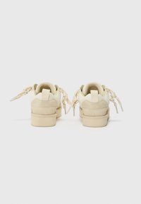 Crème-kleurige sneakers met een gladde leren en zachte textiel bovenkant, voorzien van achterste lusjes en unieke veters voor een opvallend ontwerp.