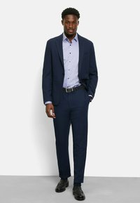 Navy suit with a fitted blazer and trousers, paired with a light blue patterned shirt, black belt, and black dress shoes.