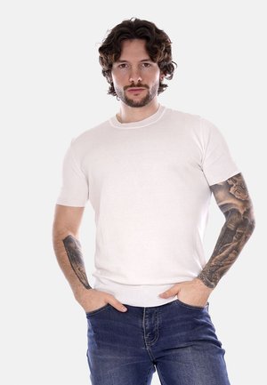T-shirt bianco a maniche corte realizzato in un tessuto morbido e elastico con un collo a coste e una vestibilità aderente, indossato con jeans blu.
