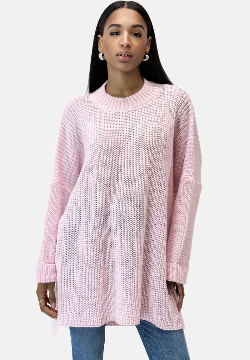 Rosa gestrickter Pullover mit einem gerippte Rundhalsausschnitt, lockerer Passform und langen Ärmeln. Besitzt ein strukturiertes Muster und seitliche Schlitze für mehr Bewegungsfreiheit.