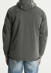 Szara kurtka z kapturem o teksturowanym wykończeniu, z detalami w postaci przeszyć i elastycznymi mankietami, noszona na jasnoniebieskich, postarzałych dżinsach.