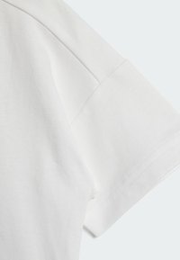 Dettaglio di una t-shirt bianca in cotone con una texture morbida, maniche corte con risvolto e rifiniture di cucitura pulite.