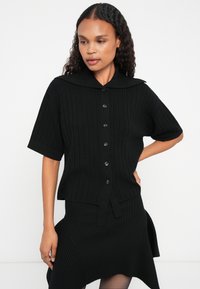 Μαύρο πλεκτό τοπ με ριμπ σχέδιο και φαρδύ γιακά, κοντά μανίκια και κλείσιμο με κουμπιά μπροστά; σχεδιασμένο για εφαρμοστή σιλουέτα με υφή.