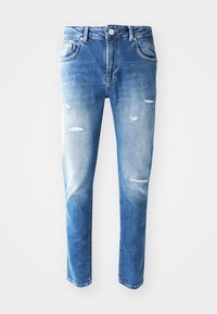 Blå denimjeans med en ljus till mörk gradient, slitna detaljer inklusive hål, fem fickor och en knappstängning vid midjan.