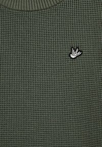 Adīts zaļš džemperis ar teksturētu rakstu, ribinātu apkakli un mazu izšūtu balto dizainu uz krūšu.