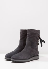 Stivaletti alla caviglia in suede grigio scuro con punta tonda, suola piatta in gomma e bottoni decorativi con dettaglio a fiocco all'esterno.