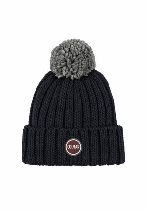 Gebreide beanie in donkerblauw met een grijze pompon bovenop. Heeft een geribbelde textuur en een rond logo-patch in rood en zilver aan de voorkant.
