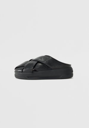 Czarna sandałka typu slip-on z grubymi, krzyżującymi się skórzanymi paskami i masywną podeszwą, z subtelnym logo "Love Moschino" po boku.