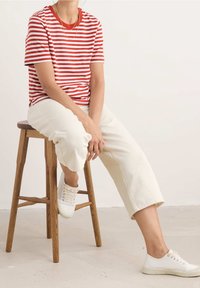 Camiseta de manga corta a rayas rojas y blancas combinada con pantalones cortos blancos y zapatillas blancas, sentado en un taburete de madera.