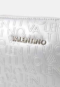 Borsetta cosmetica argentata opaca con testo in rilievo "VALENTINO" e cerniera argentata. Texture liscia con un design rettangolare elegante.