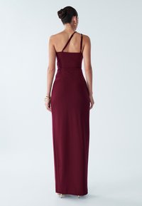 Dolga bordova obleka s prilegajočo se silhueto, nastavljivimi tankimi naramnicami in stranskim razporkom. Izdelana iz gladkega blaga z dolžino do tal.