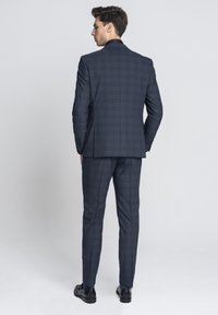 Granatowy garnitur w kratę o dopasowanym kroju, z pojedynczym rozcięciem, dwoma guzikami i eleganckimi spodniami, uzupełniony błyszczącymi czarnymi butami.