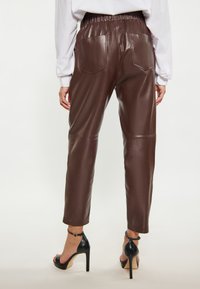 Bruine faux leren broeken met een hoge taille, elastische band en twee achterzakken. Gestyld met zwarte hoge hakken sandalen.