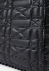 Sac en cuir noir matelassé avec une surface texturée, présentant des motifs de couture diagonaux et verticaux pour plus de détails.