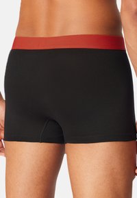 Boxer aderenti neri con un elastico rosso in vita, realizzati in un tessuto morbido, progettati per comfort e flessibilità.