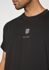 Schwarzes Baumwoll-T-Shirt mit rundem Halsausschnitt und kurzen Ärmeln, mit weißem USA-Logo und dem Text "FOREVER FORWARD" auf der Brust.