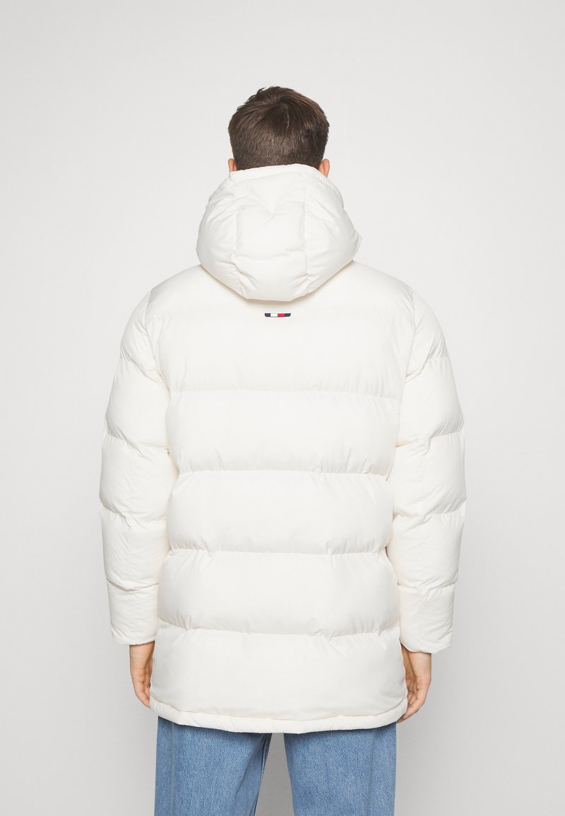 Chaqueta tipo puffa blanca con capucha, con un diseño acolchado y acolchado visible. Destacado detalle de logo en rojo, blanco y azul en la parte posterior.