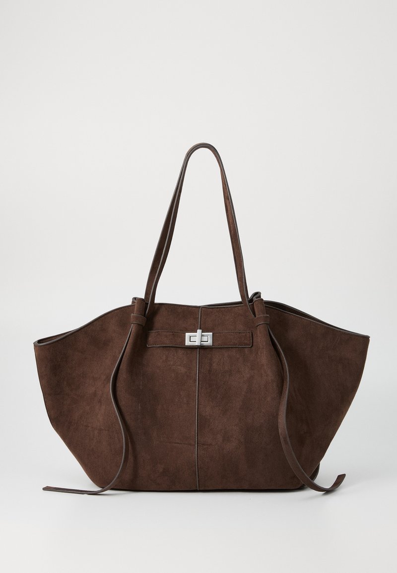 Brun mockaskinns toteväska med en bred, strukturerad form, dubbla handtag och ett spänne i silverfärg i mitten. Texturerad yta med minimala detaljer.