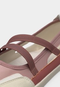 Ελαφρώς ροζ παντόφλα με δύο ελαστικούς ιμάντες στην κορυφή και μπεζ στρογγυλεμένη μύτη με ορατή ραφή.